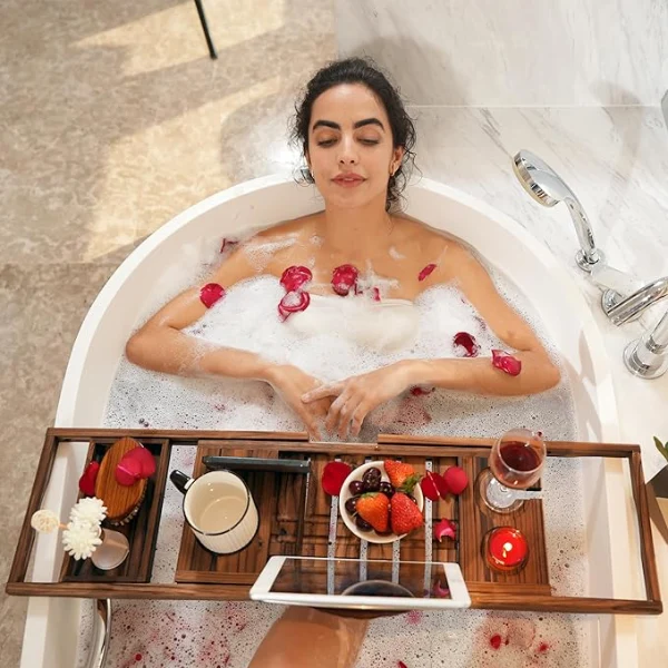 A woman is lying in the bathtub and watching iPad using bathtub tray table while taking a bath