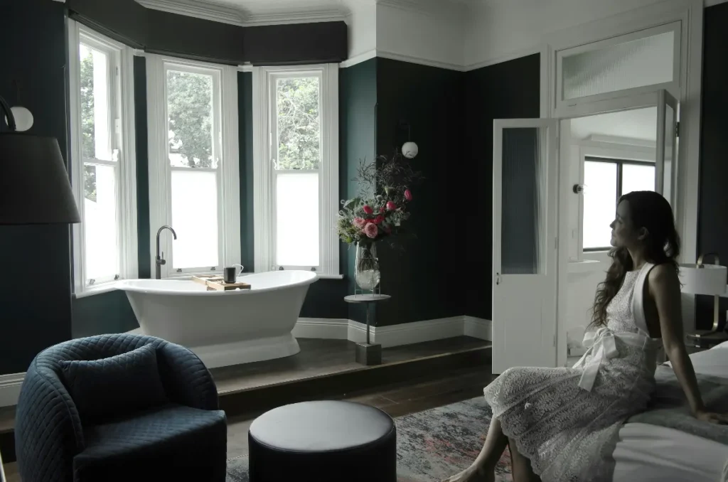 A woman is sitting on the bed with a bathtub tray table on the opposite side of the bathtub