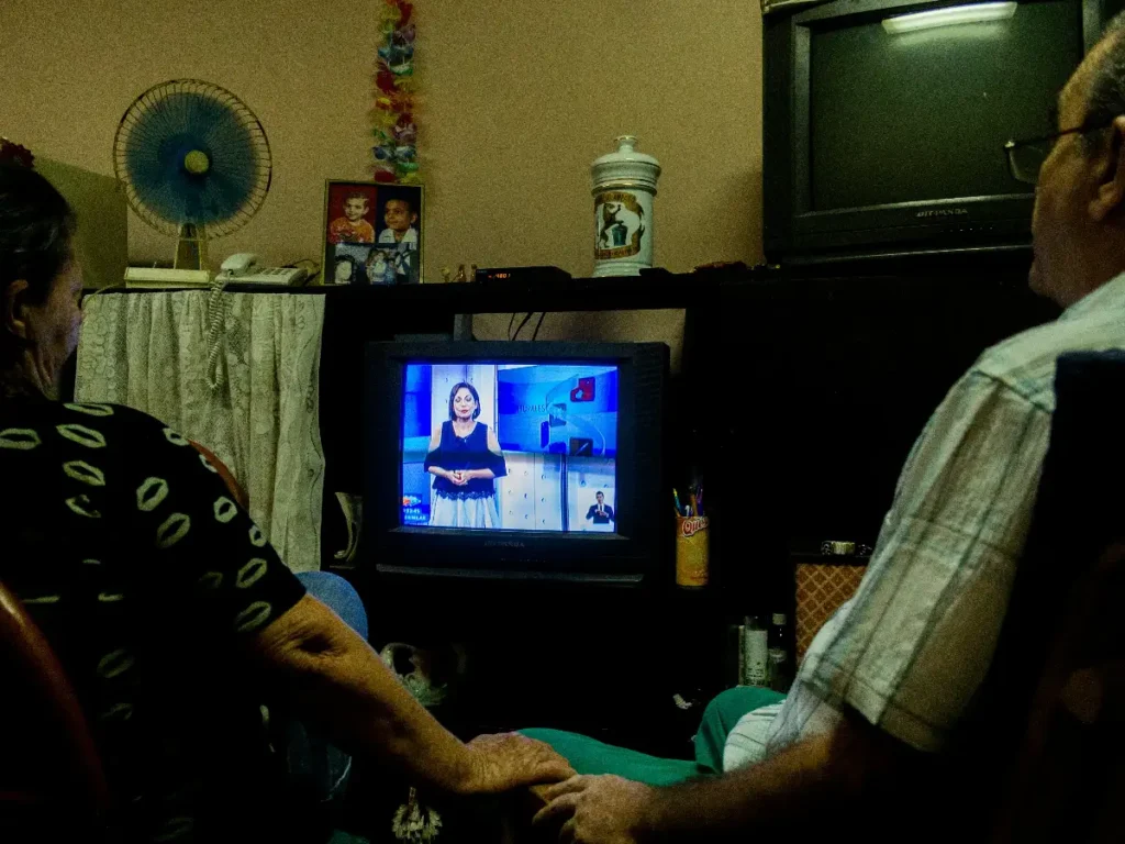 An old couple watching TV in a small living room