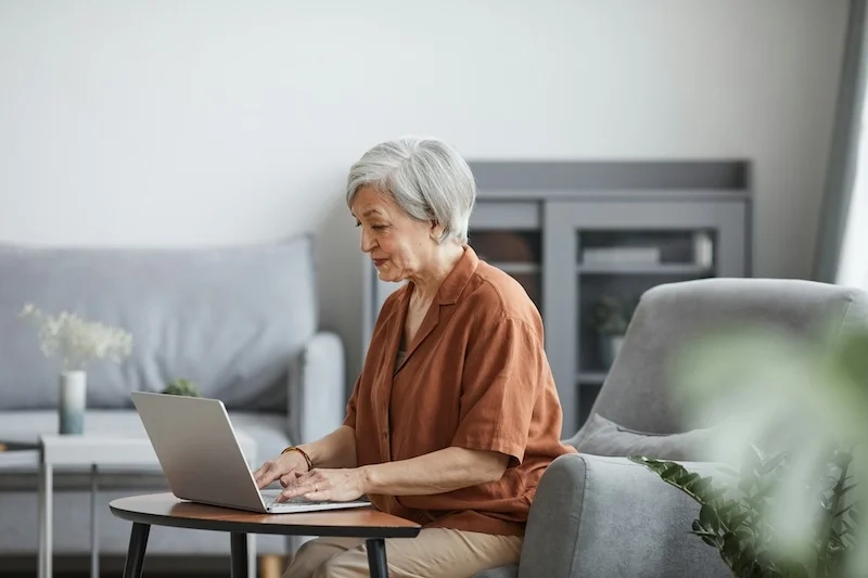 An old woman sitting on the sofa working on a computer